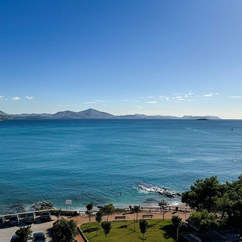 A breathtaking view of the sea in Varkiza, Greece, with clear blue waters and a rocky shoreline under a sunny sky
