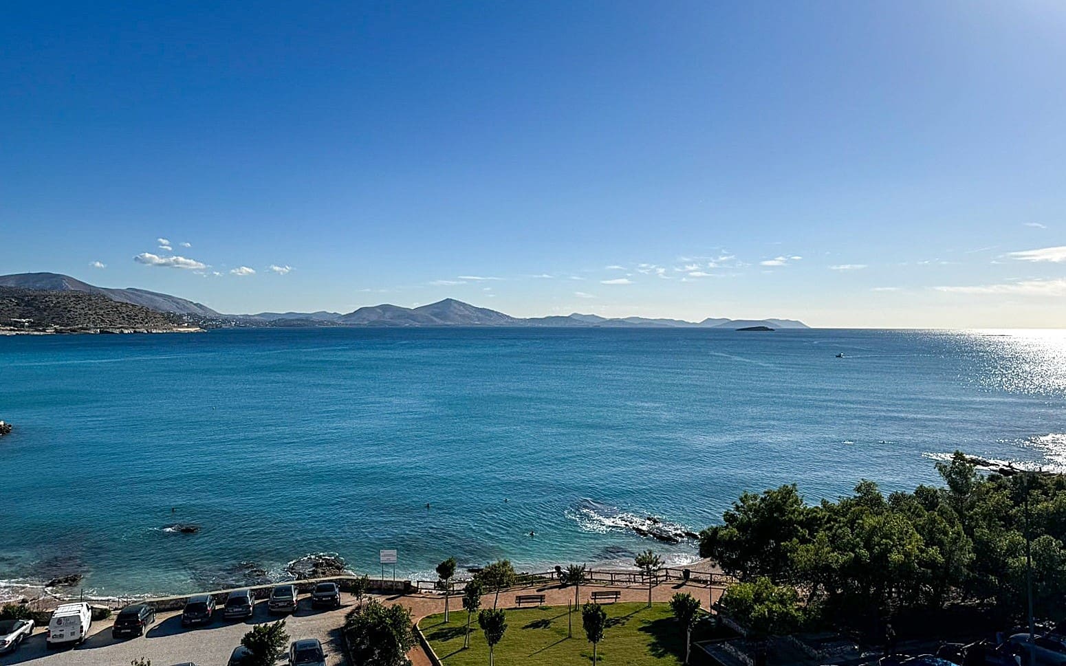 A breathtaking view of the sea in Varkiza, Greece, with clear blue waters and a rocky shoreline under a sunny sky