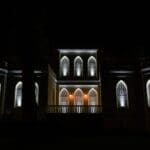 The illuminated façade of the historical estate in Peloponnese at night, highlighting its Gothic and Neoclassical architecture against the starry sky