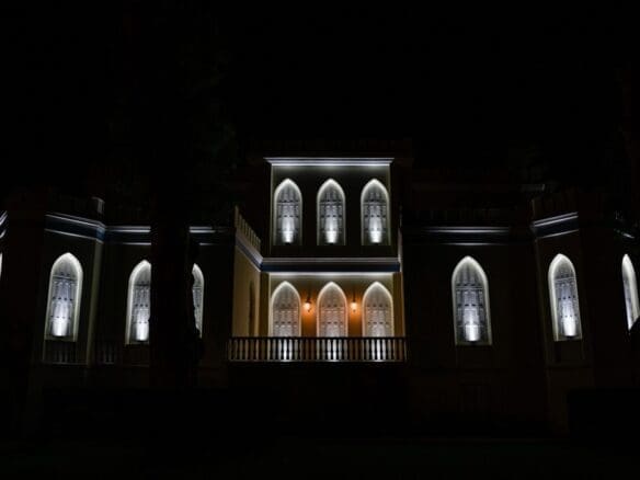 The illuminated façade of the historical estate in Peloponnese at night, highlighting its Gothic and Neoclassical architecture against the starry sky